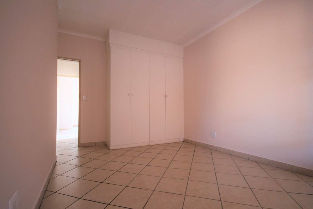 An empty bedroom featuring neutral tiled flooring and built-in cupboards, offering a clean and versatile space ready for personalization.