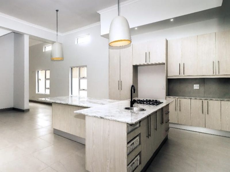 Modern open-plan kitchen featuring light wood cabinetry, stone countertops, a central island with a gas hob, and sleek pendant lighting.