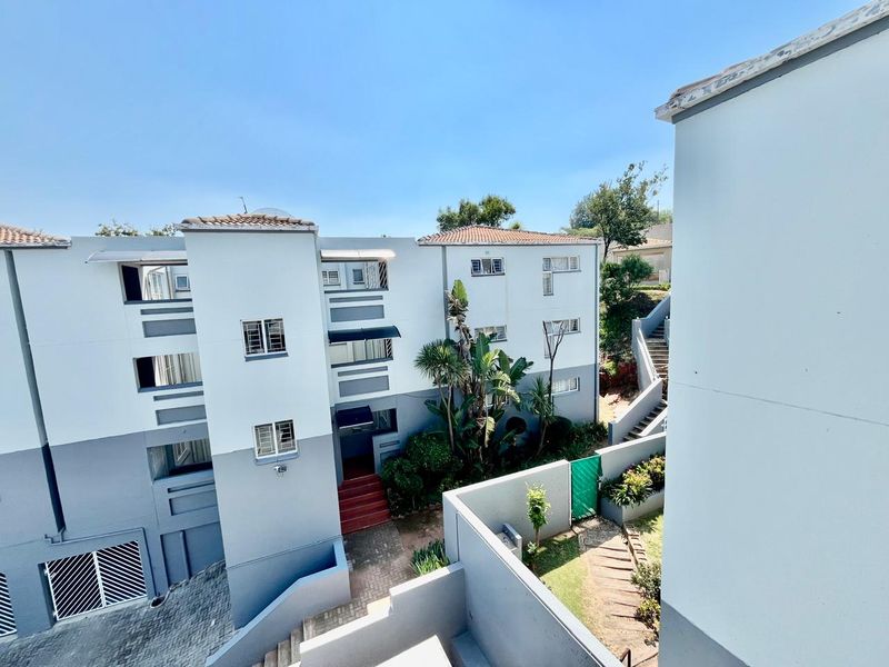 An elevated view of the apartment complex exterior, featuring paved walkways, concrete staircases, and landscaped garden areas between the building blocks.
