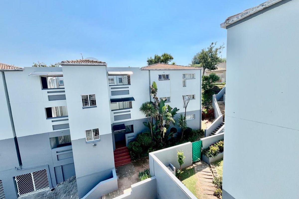 An elevated view of the apartment complex exterior, featuring paved walkways, concrete staircases, and landscaped garden areas between the building blocks.