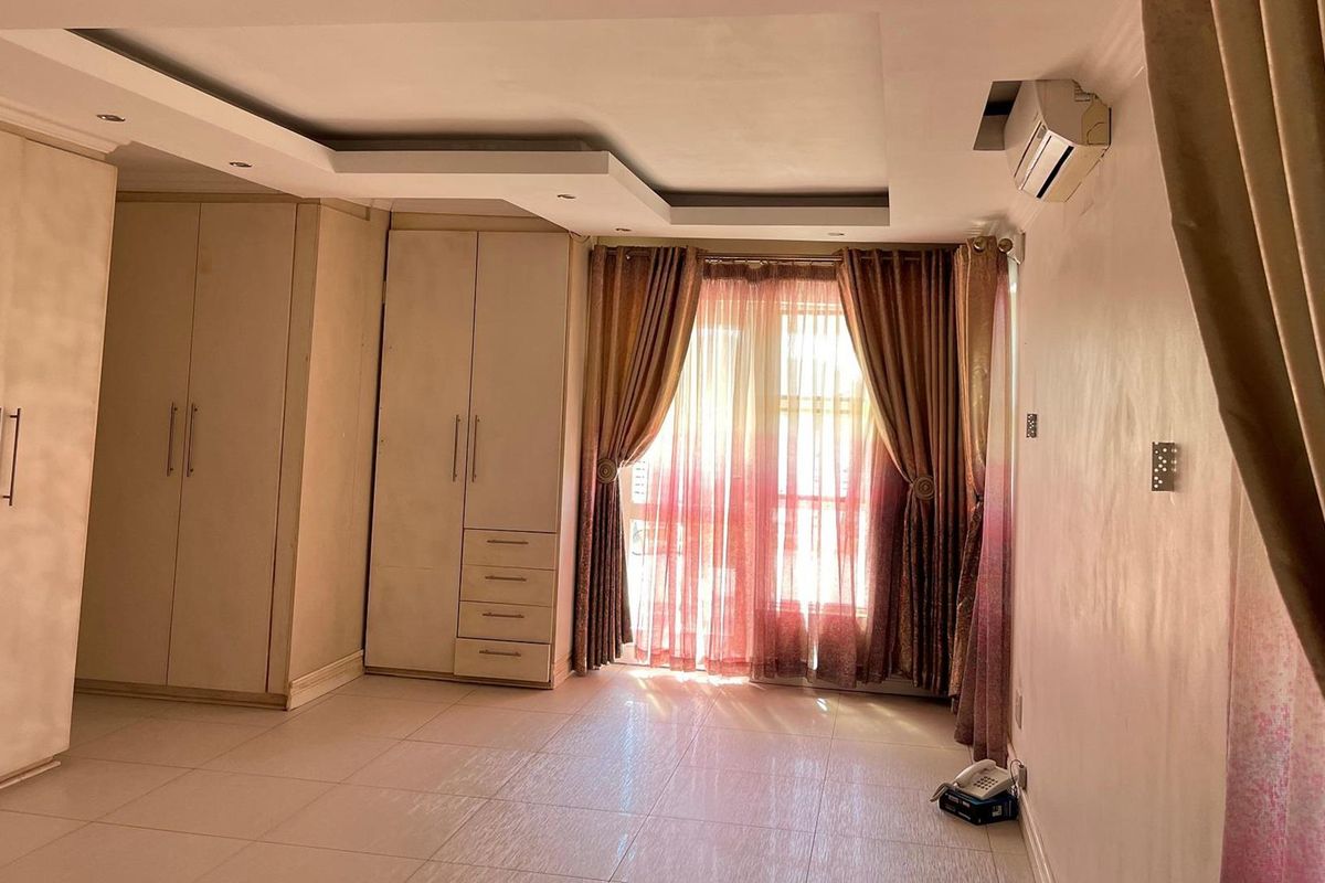 A spacious bedroom featuring extensive built-in cabinetry, tiled flooring, a recessed ceiling design, and a wall-mounted air conditioning unit.