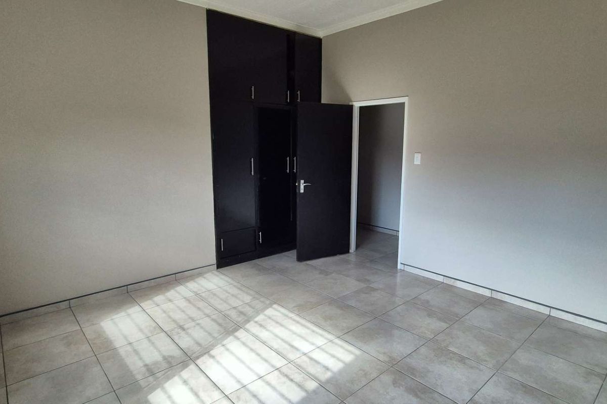 A spacious bedroom featuring neutral tiled flooring and built-in dark cabinetry, offering a clean and functional living space.