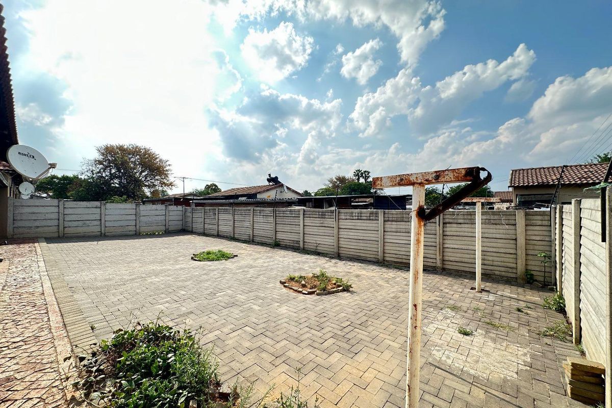 A spacious paved backyard area enclosed by precast concrete boundary walls, featuring a central washing line structure and small garden beds.