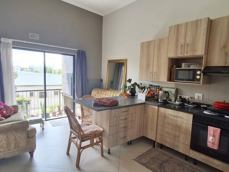 Open-plan living area featuring a modern kitchen with wood-finish cabinetry, built-in appliances, and direct access to a balcony through sliding glass doors.