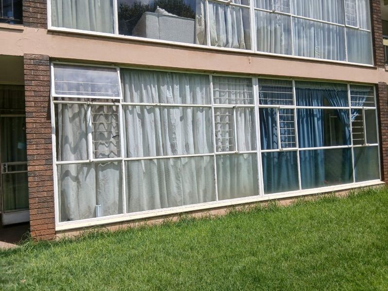 Exterior view of the apartment building featuring large multi-pane windows with security bars and brick facade detailing.