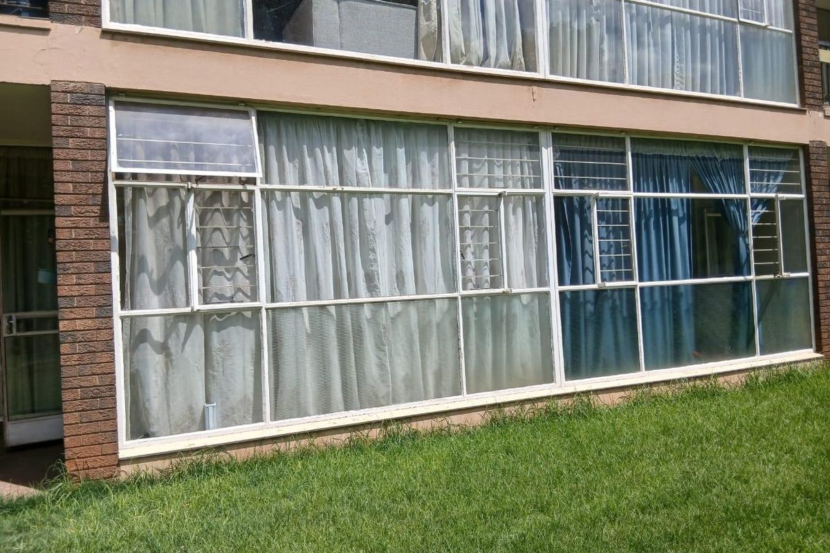 Exterior view of the apartment building featuring large multi-pane windows with security bars and brick facade detailing.