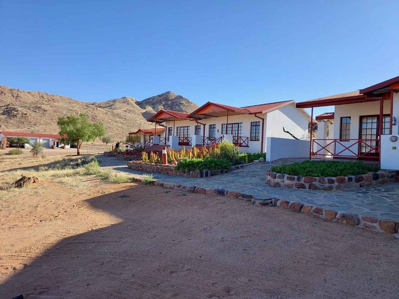 Exterior view of a row of farm-style guest units featuring covered patios, stone-paved walkways, and desert landscaping against a mountain backdrop.