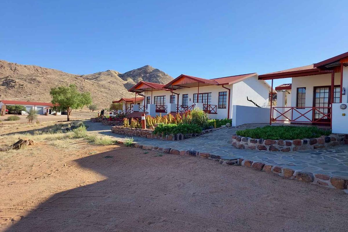 Exterior view of a row of farm-style guest units featuring covered patios, stone-paved walkways, and desert landscaping against a mountain backdrop.