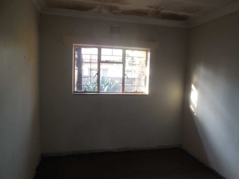An empty bedroom featuring a metal window with security bars and visible ceiling water damage requiring maintenance and cosmetic updates.
