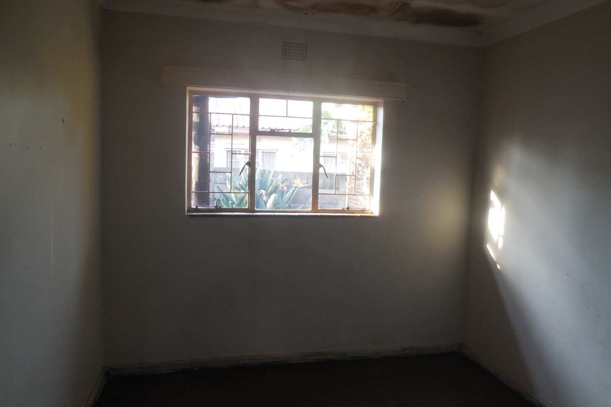 An empty bedroom featuring a metal window with security bars and visible ceiling water damage requiring maintenance and cosmetic updates.