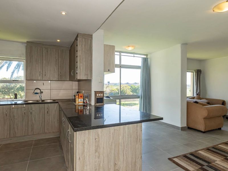 Open-plan kitchen and living area featuring modern laminate cabinetry, granite countertops, tiled flooring, and large windows providing natural light.