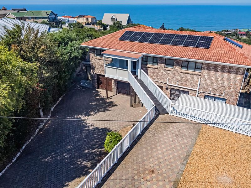 Aerial view of a brick house featuring a tiled roof with solar panels, a paved driveway, and a raised walkway leading to the entrance.