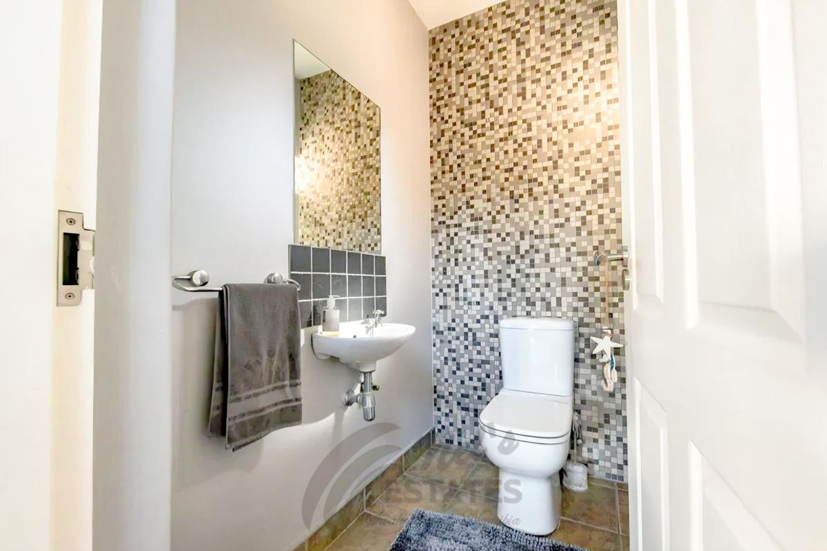 A compact guest bathroom featuring a wall-mounted basin, a modern toilet, and a decorative mosaic-tiled feature wall.
