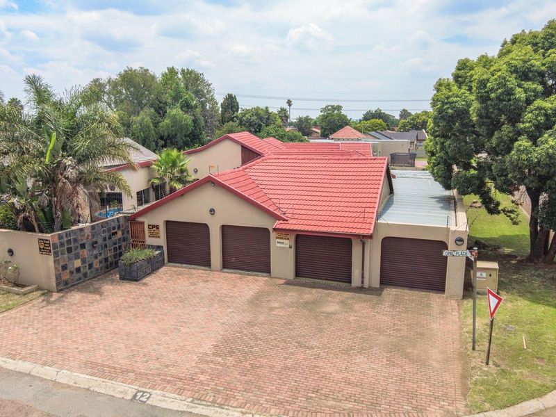 Aerial view of a residential property featuring a four-car garage configuration, paved driveway, and established boundary walls in a suburban setting.