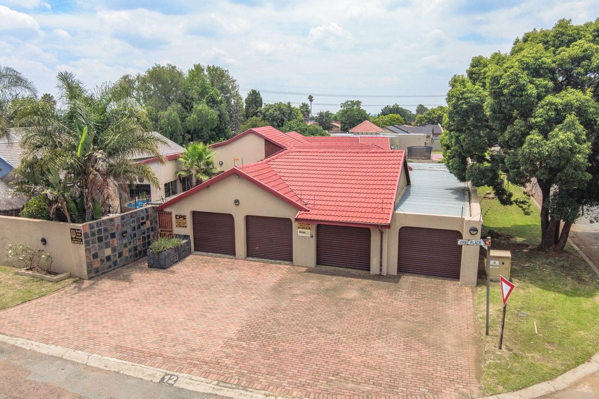 Aerial view of a residential property featuring a four-car garage configuration, paved driveway, and established boundary walls in a suburban setting.