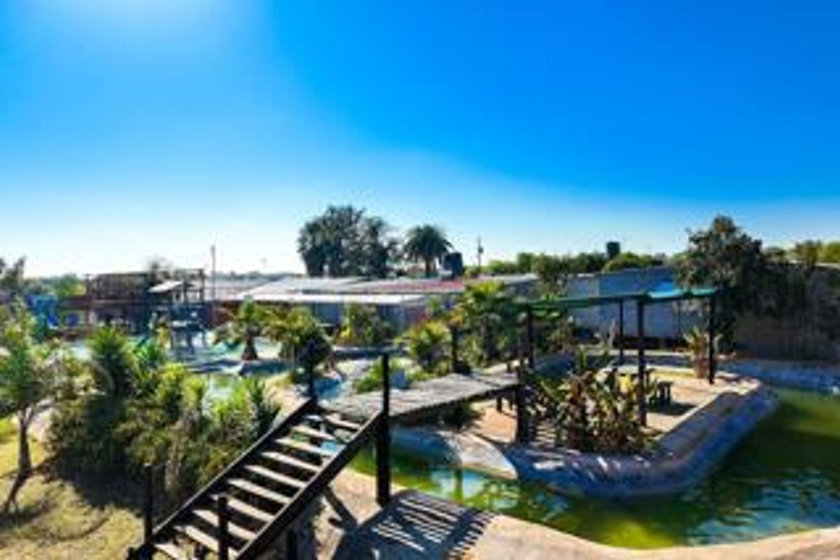 Outdoor pool area featuring a wooden bridge, pergola, and landscaped garden elements on a small holding property.