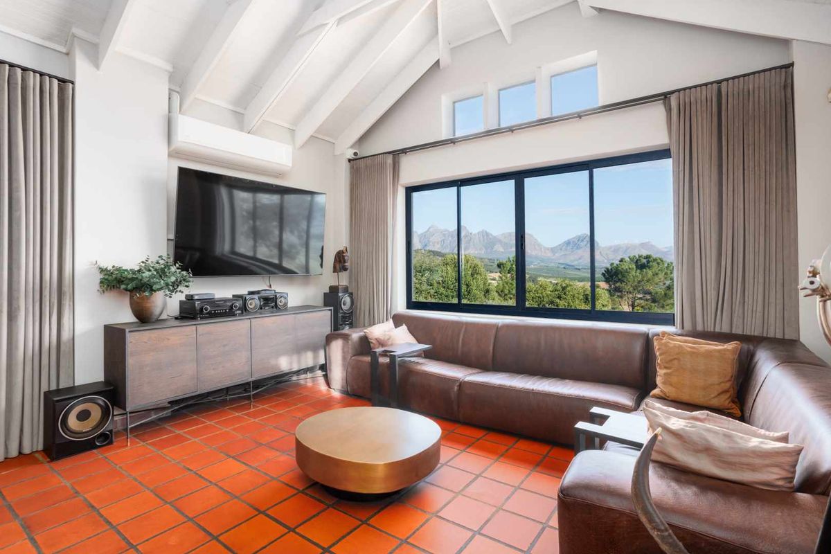 Spacious living room featuring a high vaulted ceiling with exposed rafters, terracotta tile flooring, and large windows offering scenic mountain views.
