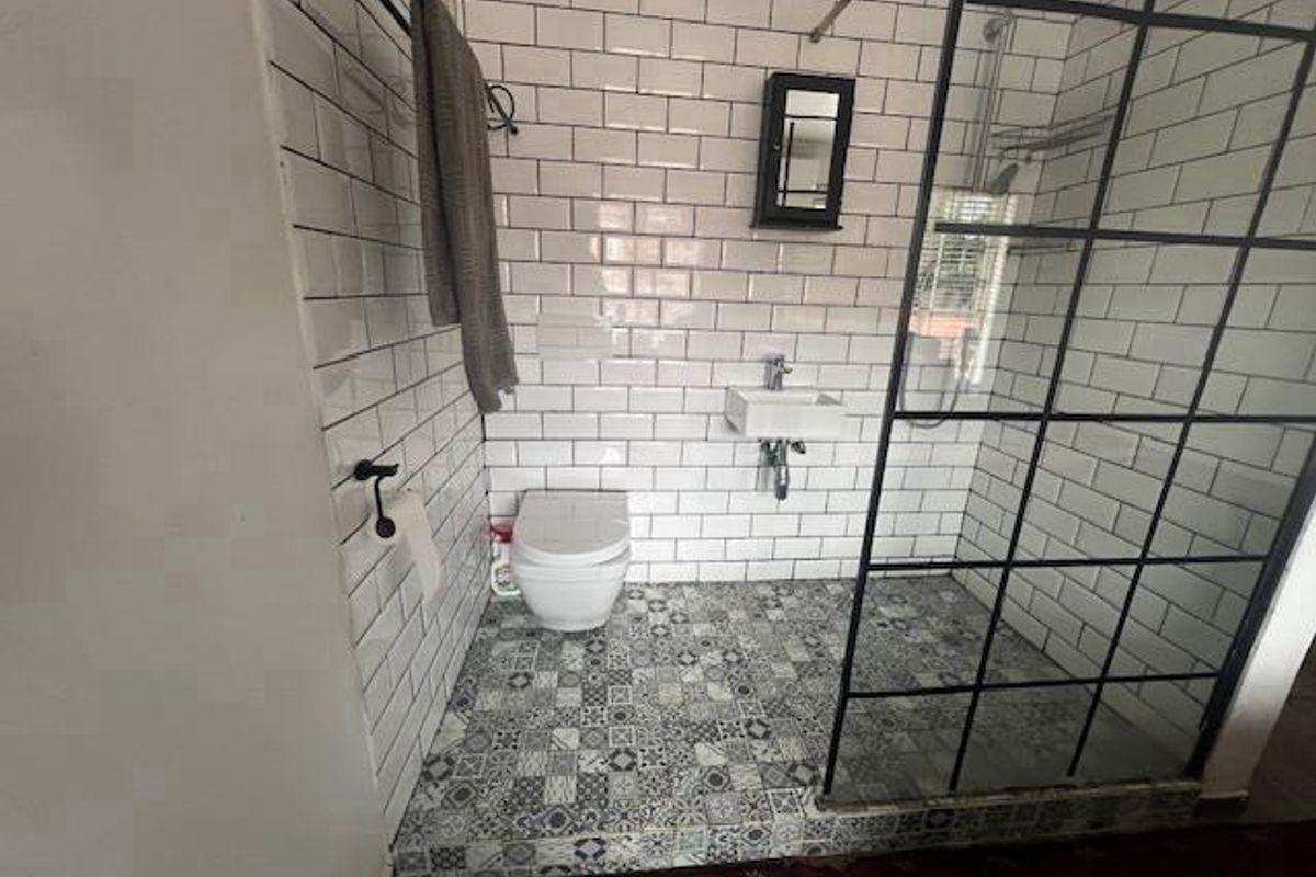 A modern bathroom featuring white subway wall tiles, patterned floor tiles, a wall-mounted toilet, a small basin, and a black-framed glass shower enclosure.