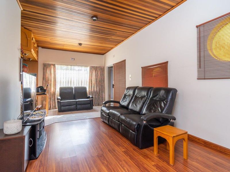 A living room featuring a warm timber tongue and groove ceiling, laminate flooring, and built-in cabinetry, offering a classic and functional living space.