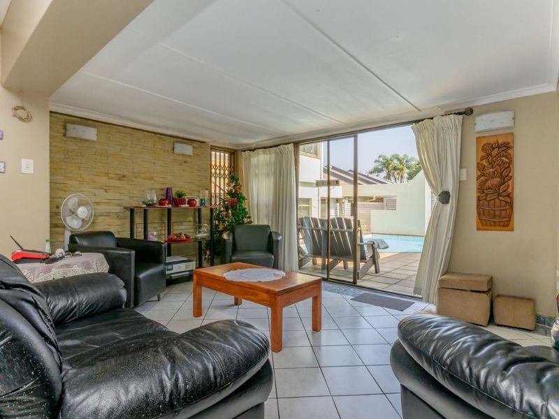 A comfortable living room featuring tiled flooring, a textured stone accent wall, and large sliding glass doors providing direct access to the outdoor pool area.