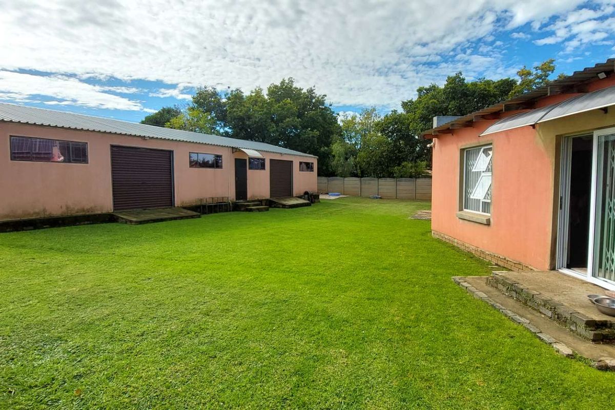 Spacious rear garden area featuring a large lawn, a detached outbuilding with roller doors, and a patio entrance to the main house.