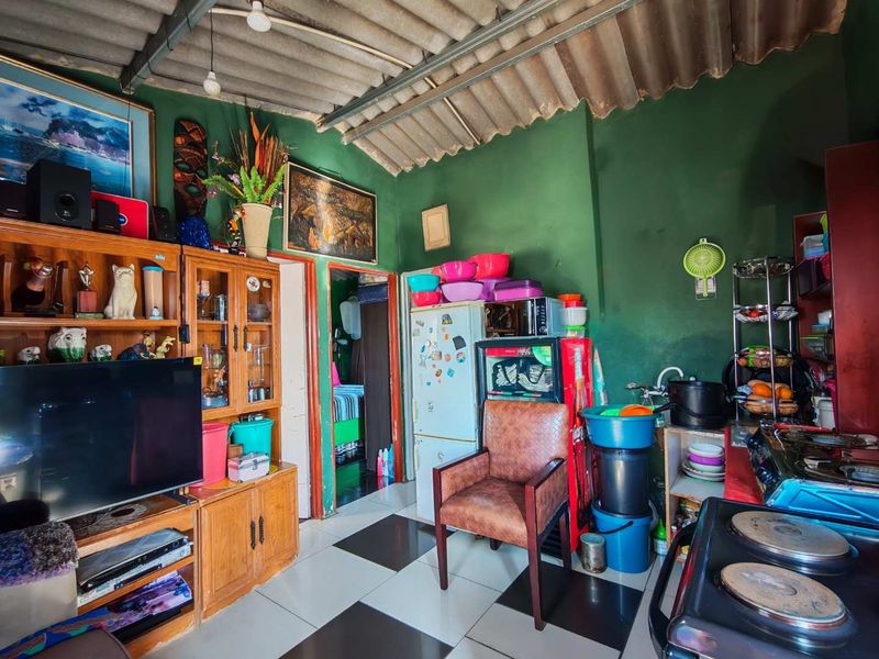 Open plan living and kitchen area featuring tiled flooring and exposed roof structure, offering a functional layout with potential for modernization.