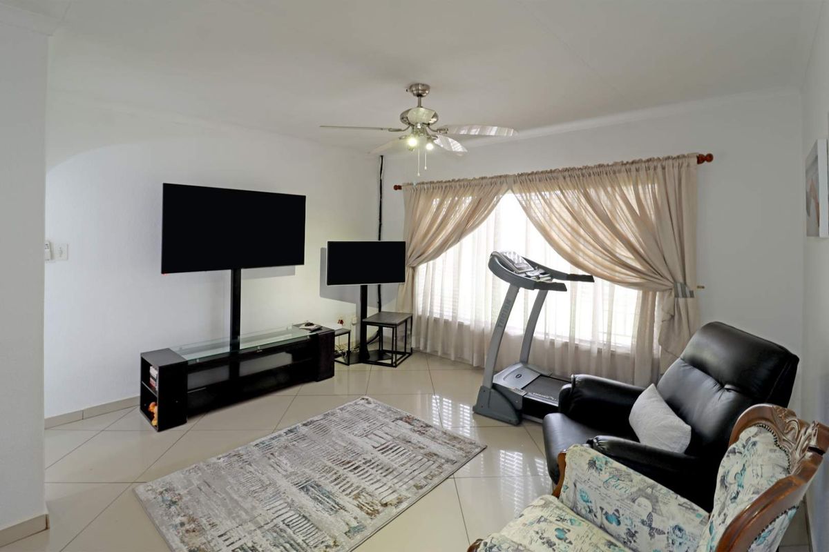 A living room featuring tiled flooring, a ceiling fan, and large windows with curtains, providing a functional space for relaxation and exercise.