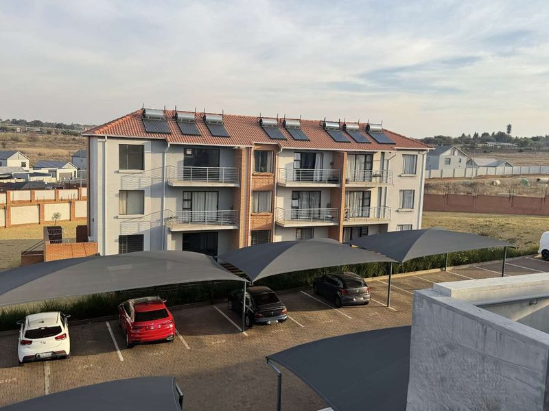 Aerial view of an apartment complex featuring a tiled roof with solar panels, private balconies, and covered parking bays.