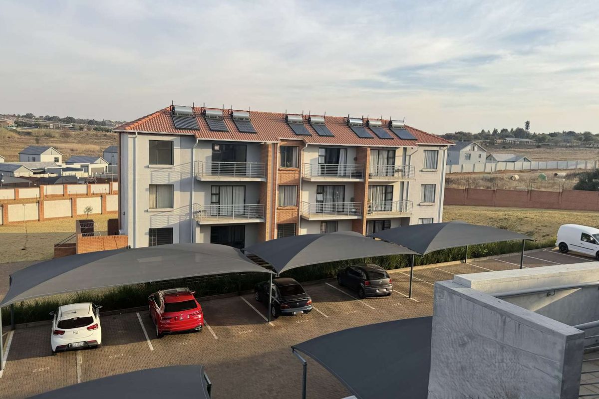 Aerial view of an apartment complex featuring a tiled roof with solar panels, private balconies, and covered parking bays.