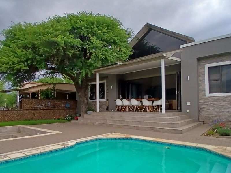 A well-maintained outdoor entertainment area featuring a swimming pool, a covered patio with bi-fold doors, and attractive stone cladding on the exterior walls.