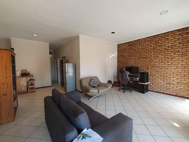 Spacious living area featuring a prominent exposed brick wall, neutral tiled flooring, and recessed lighting, offering a versatile open-plan layout.