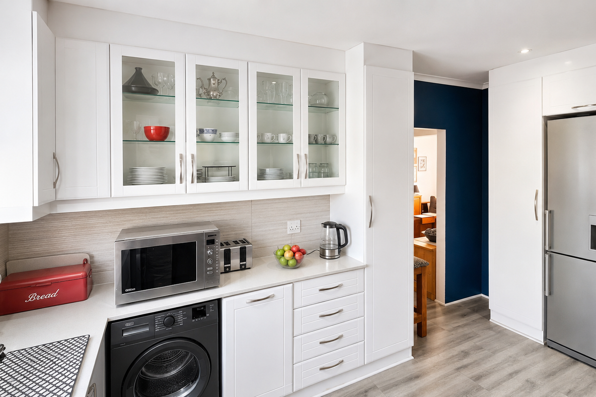 Modern kitchen featuring white shaker-style cabinetry, glass-fronted display units, integrated appliances, and a clean tiled backsplash with neutral laminate countertops.