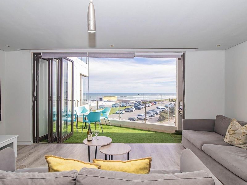 Bright living room featuring large bi-fold doors that open onto a balcony with scenic coastal views and modern laminate flooring.