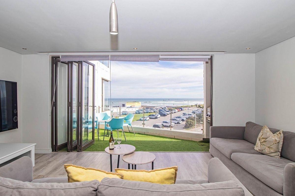 Bright living room featuring large bi-fold doors that open onto a balcony with scenic coastal views and modern laminate flooring.