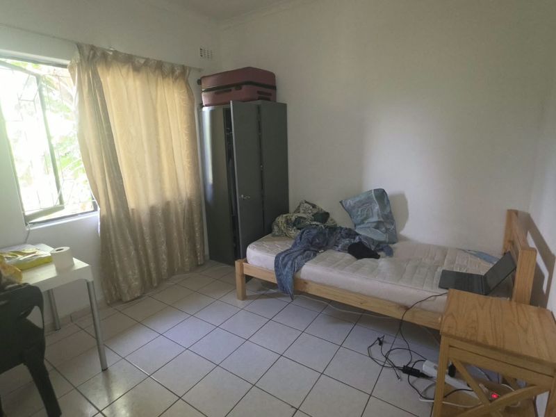 A functional bedroom featuring tiled flooring and a window with security bars, offering a simple and practical living space.