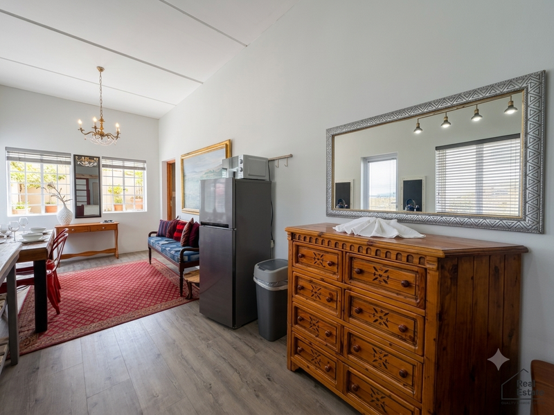 A bright living area featuring laminate flooring, neutral walls, and large windows with venetian blinds, offering a clean and well-maintained space.