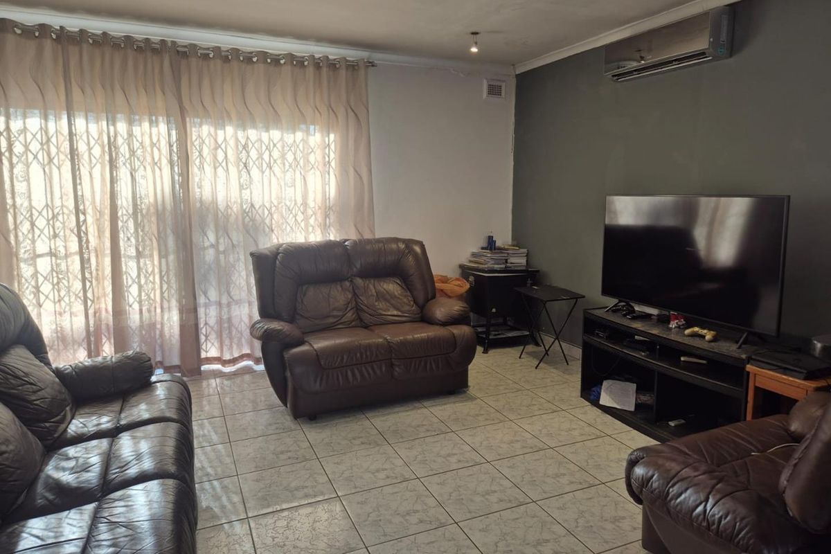 A living room featuring tiled flooring, a wall-mounted air conditioning unit, and large sliding glass doors with security gates.