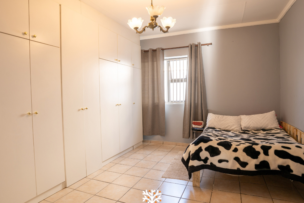A bedroom featuring extensive built-in cupboards, tiled flooring, and a window fitted with security bars.