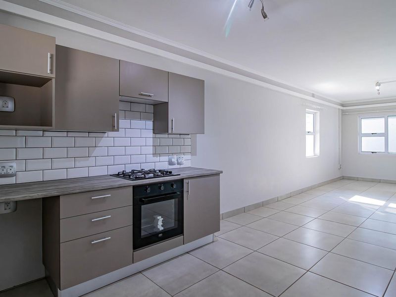 Modern open-plan kitchen and living area featuring neutral cabinetry, subway tile backsplash, built-in oven and hob, and clean tiled flooring throughout.