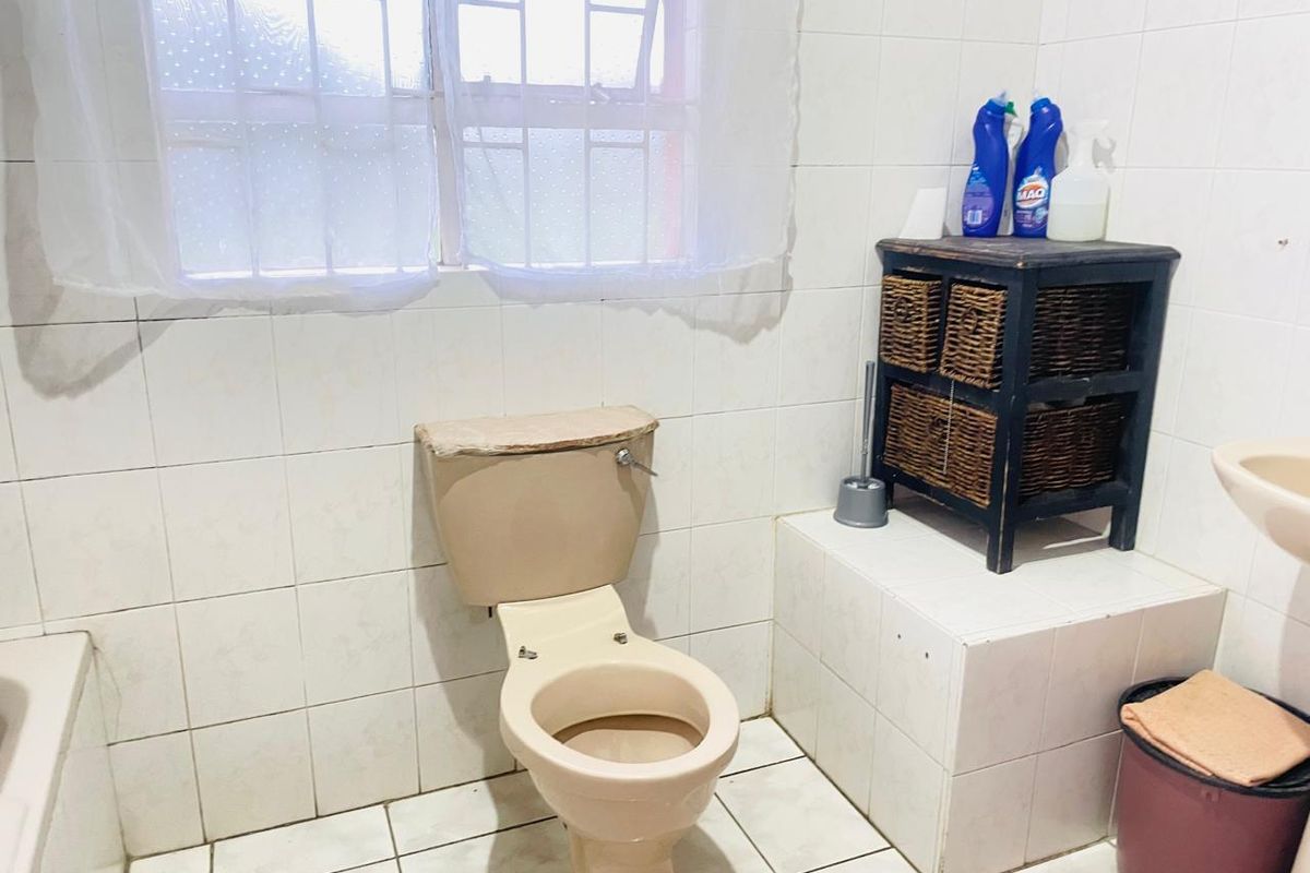 A functional bathroom featuring white wall and floor tiles, a standard toilet, and a built-in tiled vanity base.