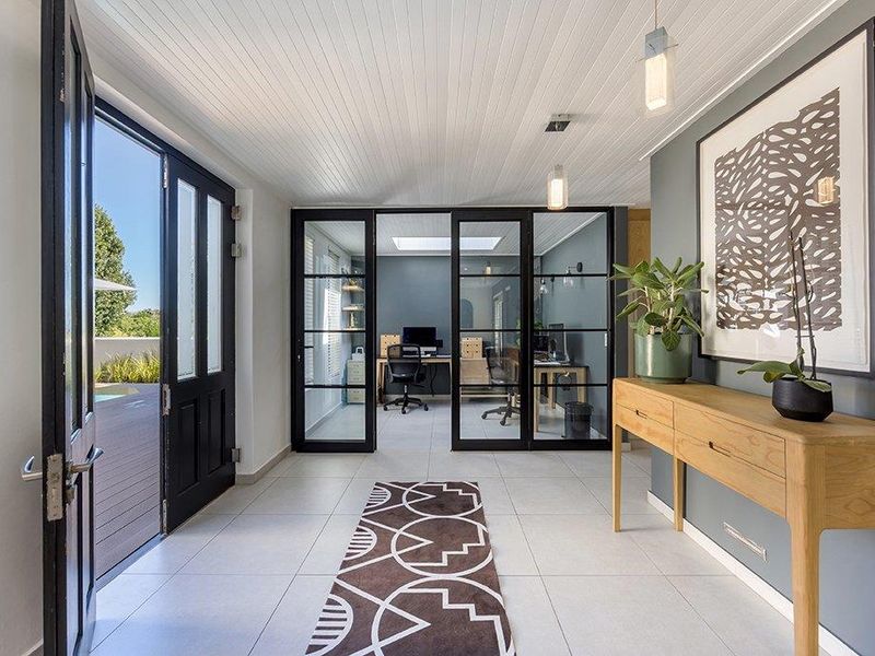 Bright and modern entrance hall featuring tiled flooring, tongue and groove ceiling, and stylish black-framed glass doors leading to an office space.