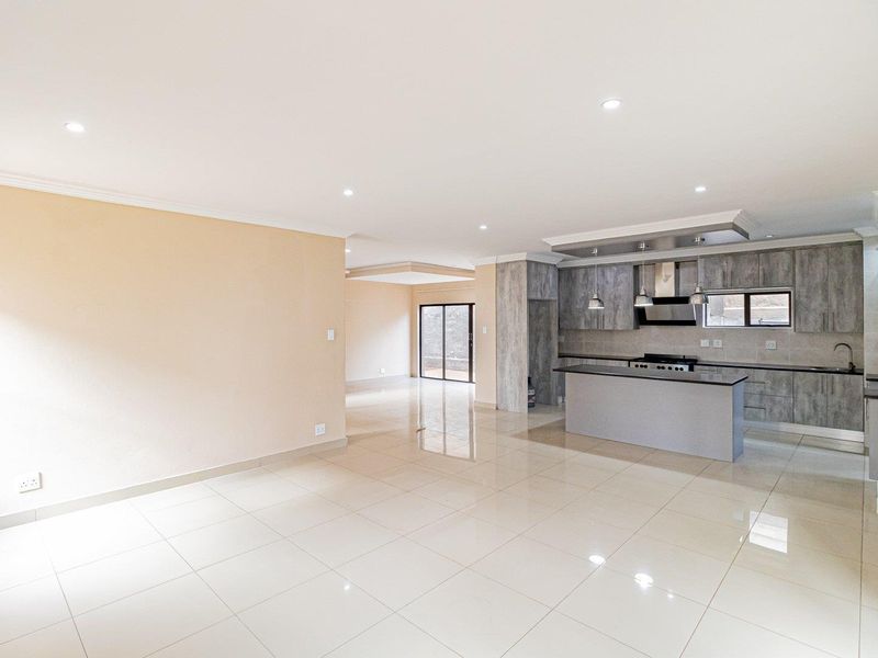 Spacious open-plan living area featuring polished porcelain tiles, recessed lighting, and a modern kitchen with stone countertops and integrated appliances.