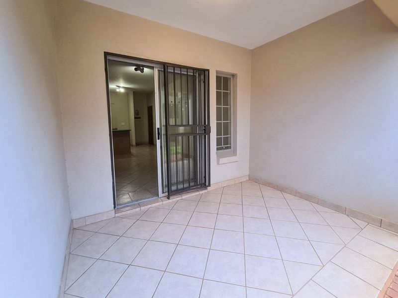 A clean, covered patio area featuring tiled flooring, a sliding glass door with a security gate, and access to the interior living space.