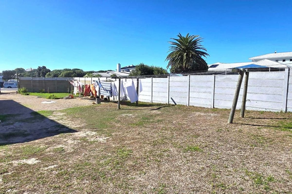 A spacious rear outdoor area featuring a large lawn, gravel driveway section, and perimeter concrete boundary walling.
