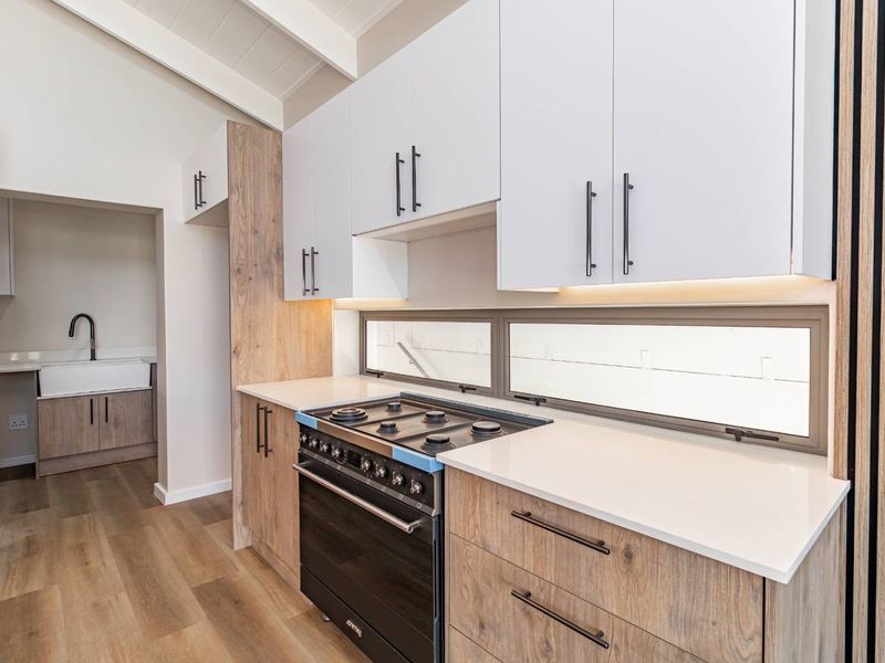 Modern kitchen featuring white and wood-grain cabinetry, quartz countertops, a gas hob, and an integrated scullery area with a farmhouse sink.