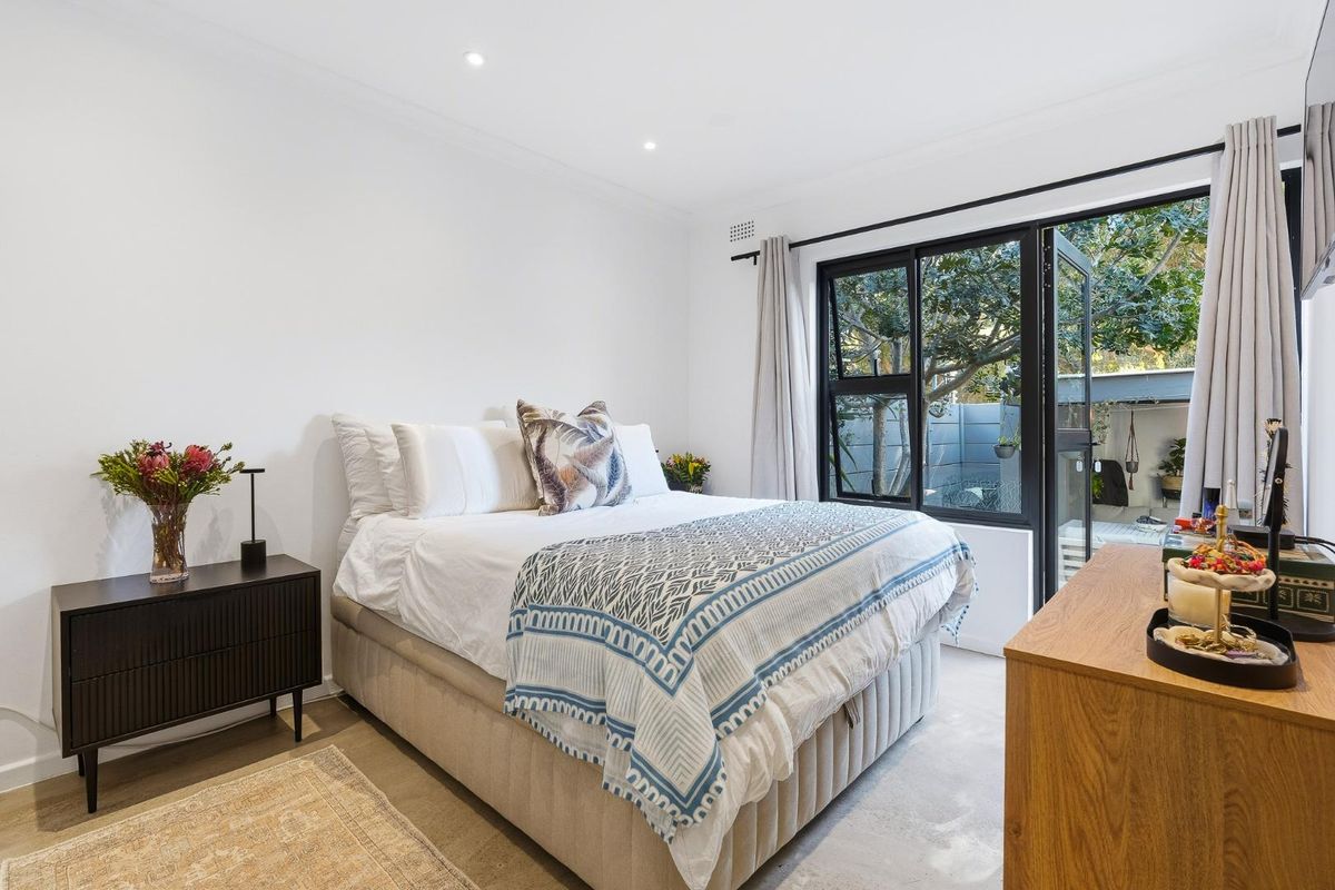 A bright and well-maintained bedroom featuring recessed downlighting and a black aluminium sliding door providing direct access to the outdoor area.