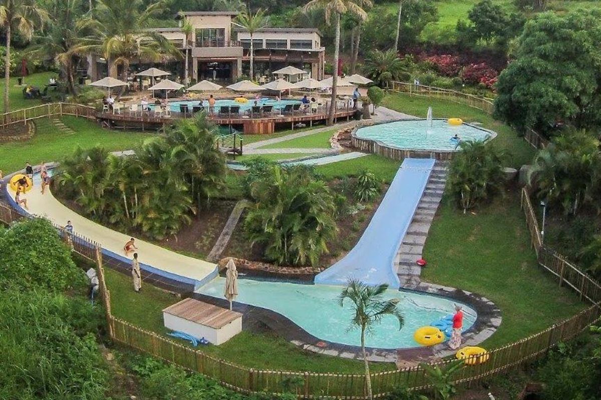Aerial view of a recreational pool area featuring multiple swimming pools, water slides, landscaped gardens, and timber decking.