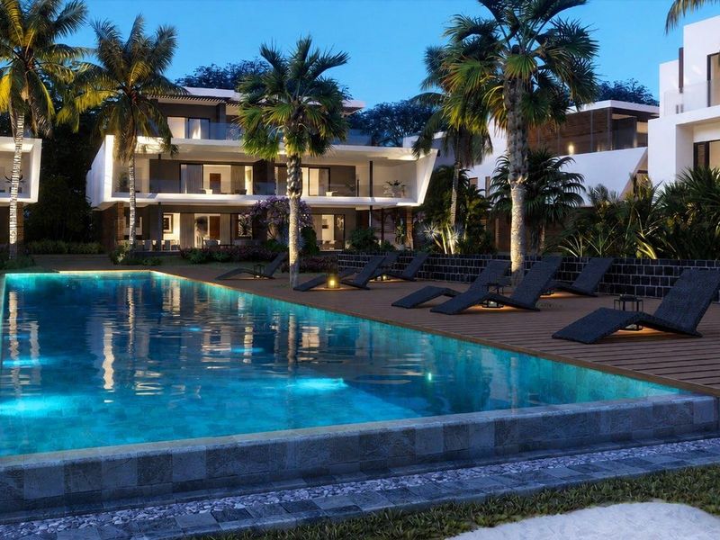 A beautifully illuminated swimming pool area featuring timber decking, stone coping, and lush landscaping, set against modern apartment architecture.