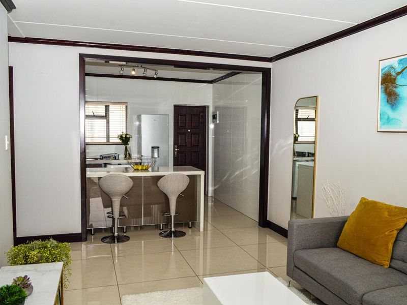Open plan living area featuring a modern kitchen island, sleek tiled flooring, and neutral finishes, creating a seamless flow between the kitchen and lounge.