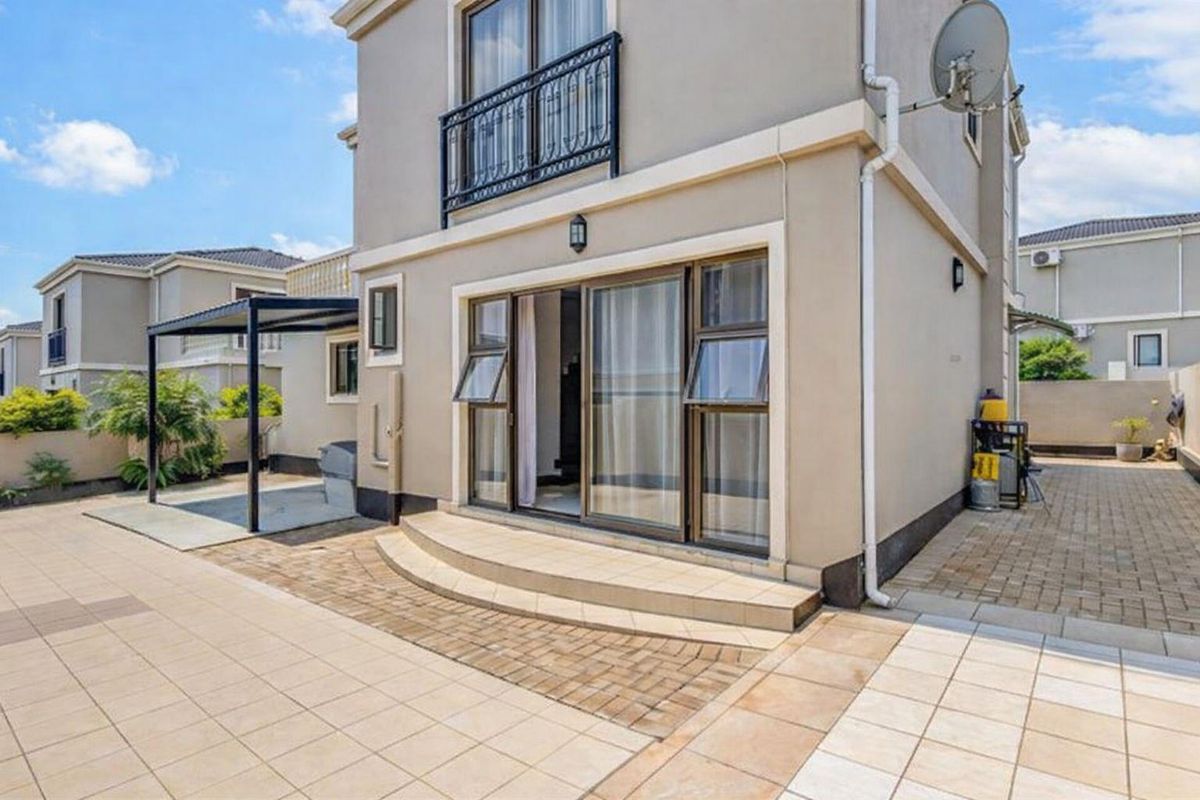 Rear view of the property featuring a paved patio area, a covered pergola, and a balcony with metal railings.
